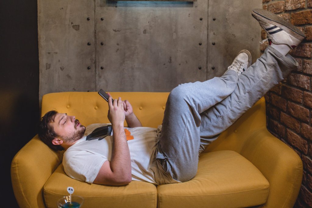 Bearded young adult with game controller lying on couch.