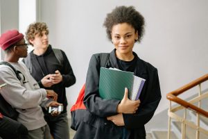 Teen girl standing in stairwell with schoolbooks in hand.