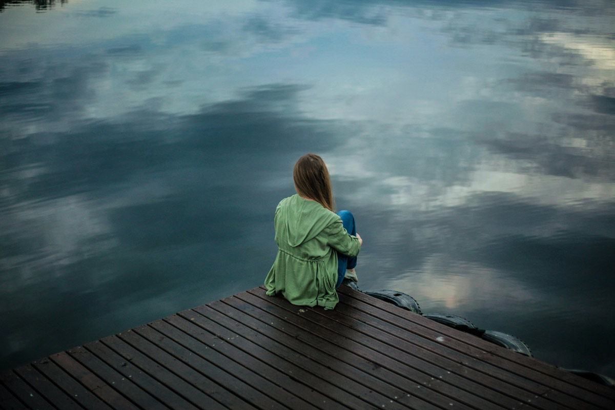 Woman sitting on dock gazing at water.