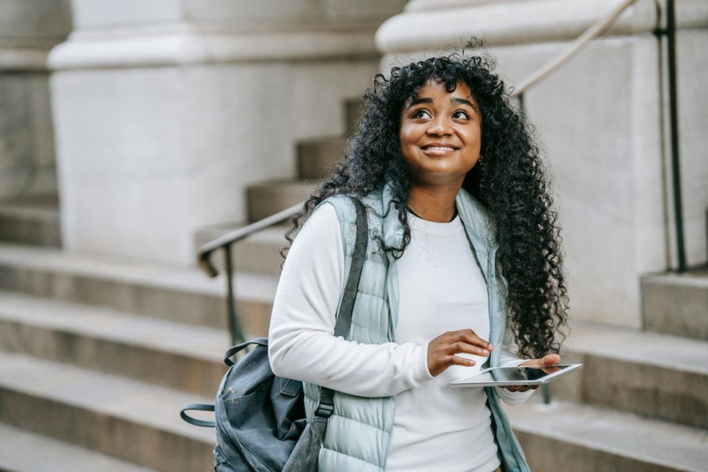 Young Black woman with tablet walking in urban setting