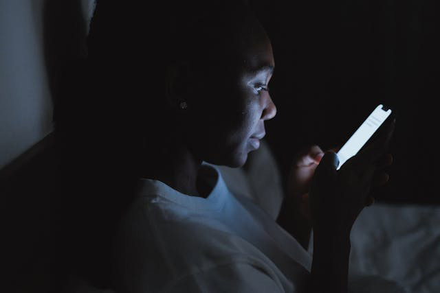 A woman sitting on her bed late at night, looking at her phone.