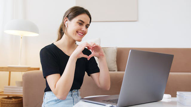 A girl making a heart with her hands in front of a laptop.