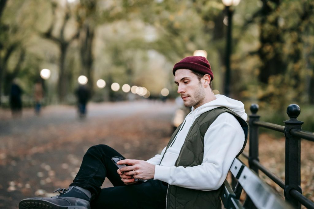 Man sitting on park bench looking at smartphone.