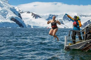 Woman jumping into mountain lake in winter.