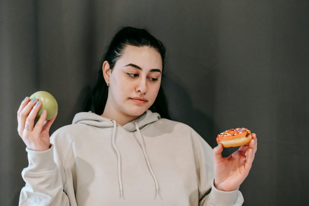 Woman trying to choose between an apple and a sugary donut.