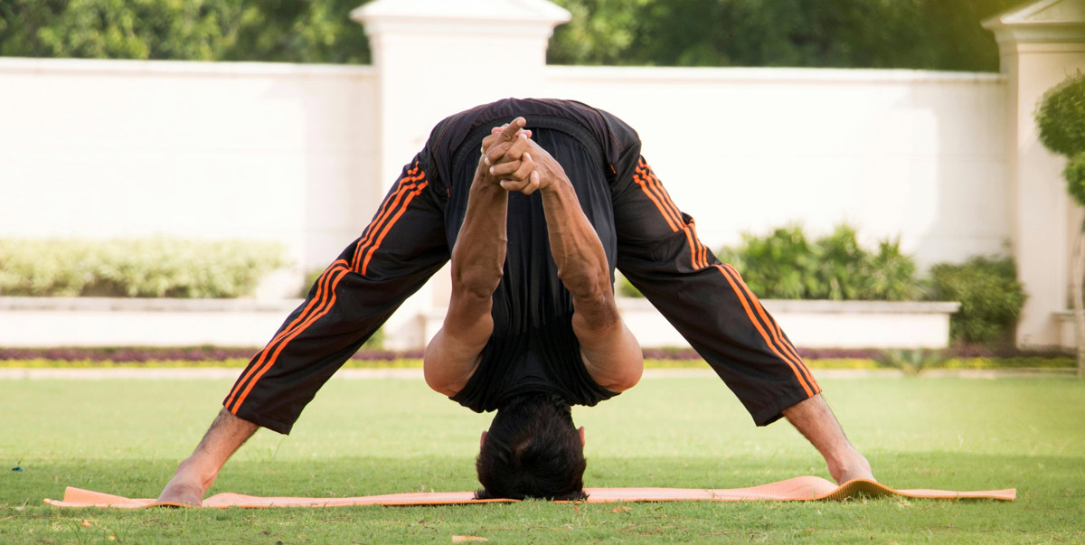 A person practicing yoga in a forward bend position on a mat, outdoors on grass.